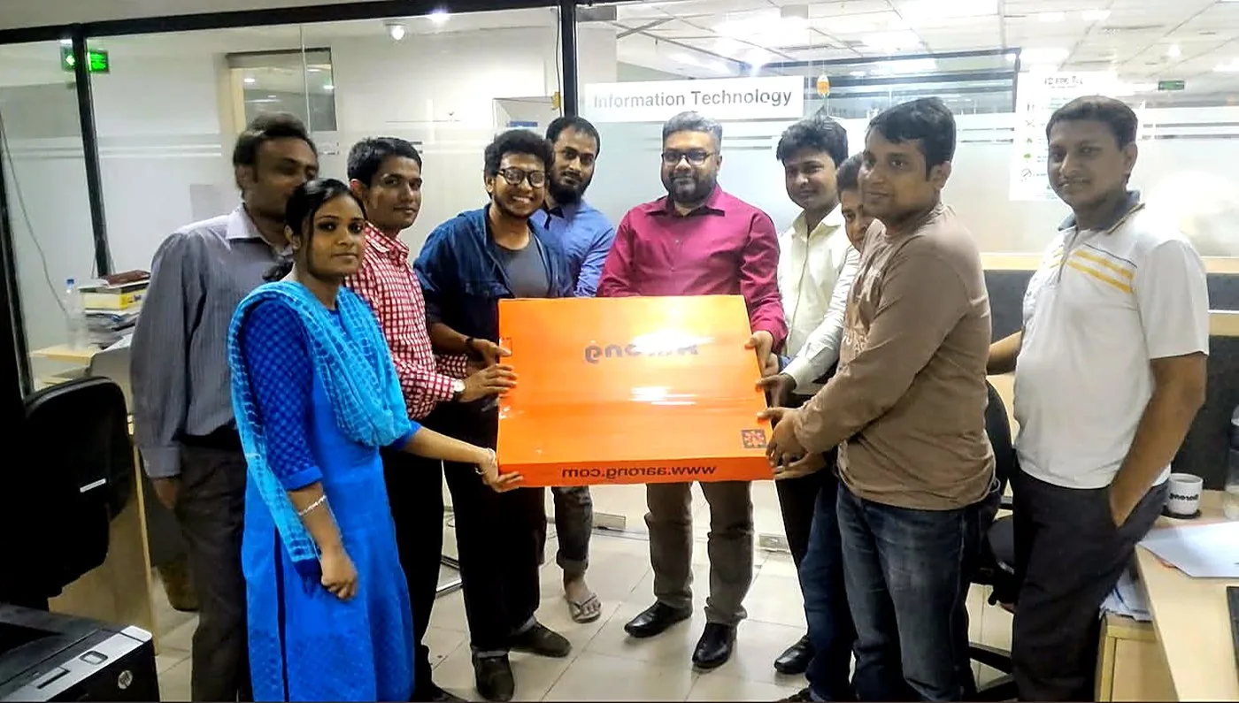 Sabbir Khan with the BRAC Aarong information technology team in their Dhaka office, the group holding an orange Aarong gift box beneath the department sign.